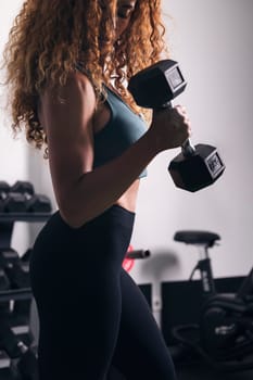crop of unrecognizable strong sportswoman doing exercise on biceps with dumbbells during workout at gym, concept of fitness and active lifestyle