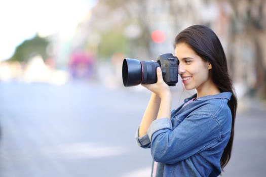 Side view portrait of a happy photographer taking photos in the street
