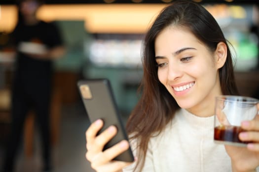 Happy customer checking cell phone holding soda in a restaurant
