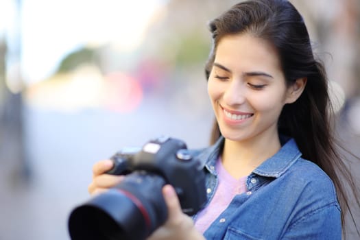 Happy photographer checking photos on camera outdoor in the street
