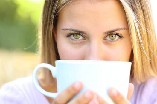 Front view portrait of a beauty woman eyes looking at you with coffee cup outdoors