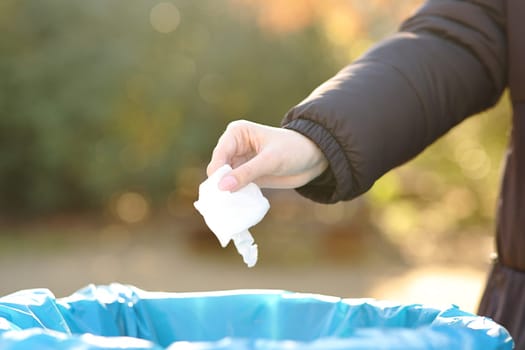 Close up of a woman hand throwing trash into paper bin in winter in a park
