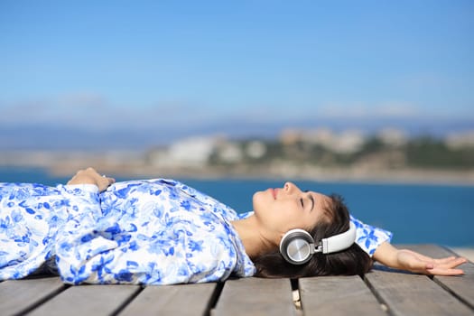 Woman relaxing listening to music with headphone lying in wooden platform on the beach