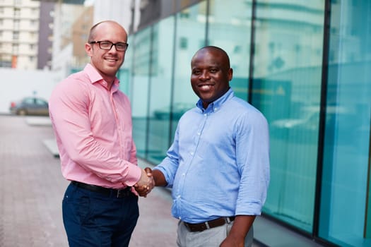 Two happy businessmen looking at camera while handshaking in urban environment