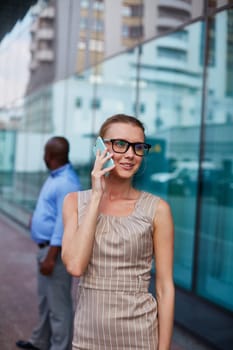 Young businesswoman in eyeglasses and casual dress speaking on the phone in urban environment