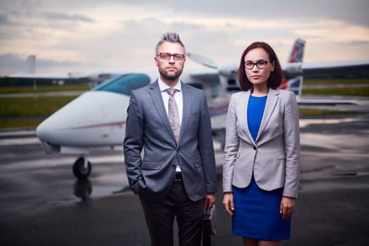 Two serious colleagues looking at camera outdoors with airplane on background