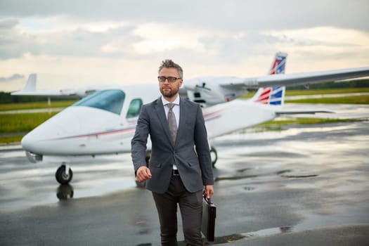Modern businessman with briefcase walking from airplane on overcast day