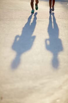 Two pairs of legs in sports-shoes and shadows of couple on asphalt road