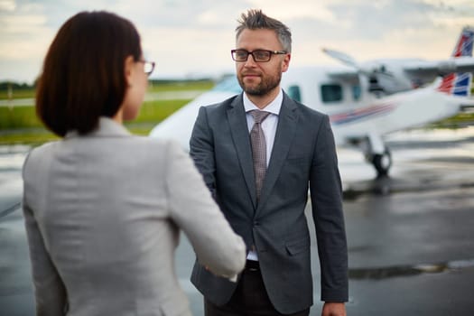 Successful businessman greeting his partner by handshake on background of airplane