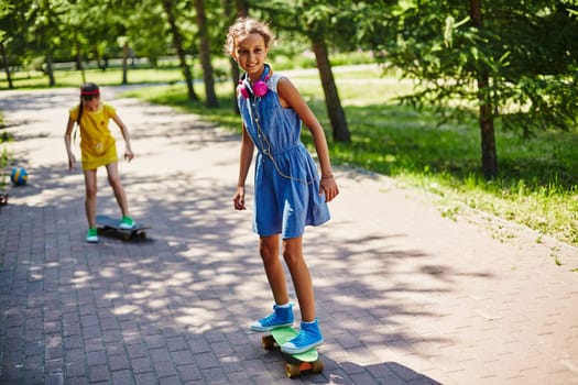 Little girl skateboarding in park with her friend on background