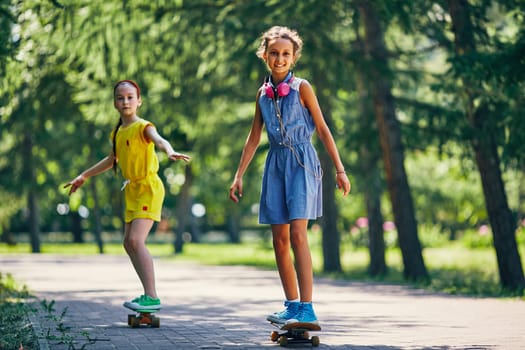 Happy cute girl and her friend skateboarding in park on summer vacations