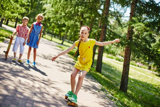 Happy girl skateboarding in park with her friends on background