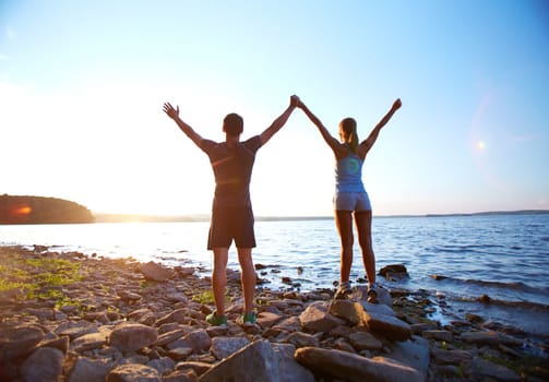 Young couple standing by the sea with raised arms