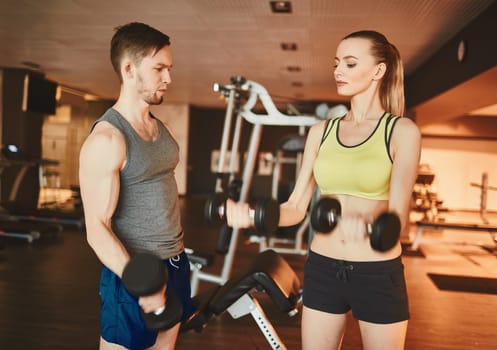 Fit woman exercising with barbells while coach consulting her