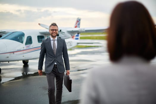 Modern businessman with briefcase walking towards his partner on background of airplane