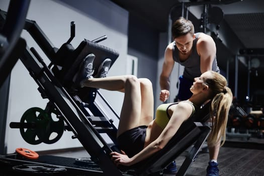 Attractive girl strengthening leg muscles on facilities while trainer encouraging her