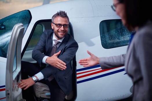 Successful businessman giving hand to his colleague while sitting in airplane