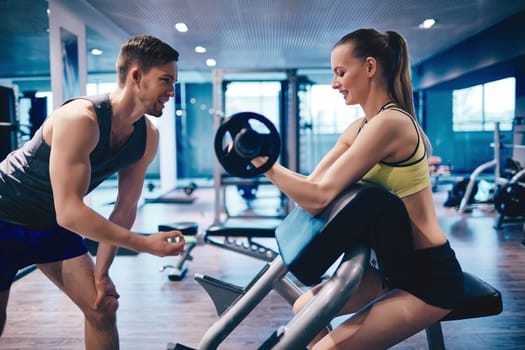Active female weightlifting in sports club, her coach consulting her