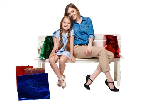 Happy  mother and daughter with shopping bags sitting at studio, isolated on white background