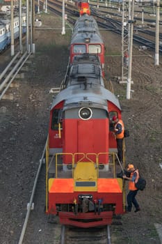 Diesel type CHME3T-7451 is on the rails at the train station. The driver with the assistant dressed in overalls, close the cabin and climb down from the locomotive. Top view of the front