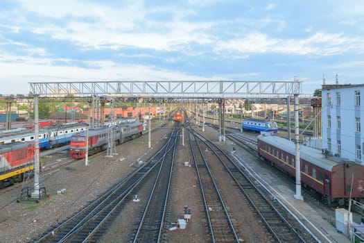 Major train station. Rails stretching into the distance. Flaw detector car is on the tracks near the building. Blue sky with a few clouds