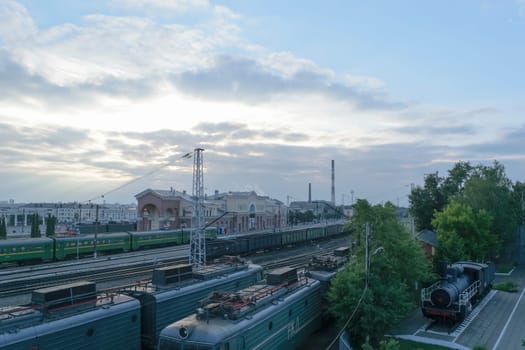 Railway Station with trains (passenger and freight) under a blue evening sky with clouds.