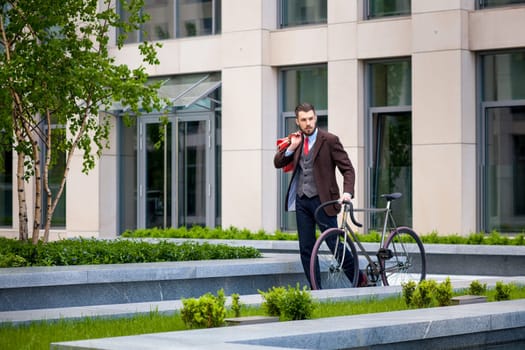 Handsome businessman in a jacket and red tie and his bicycle on city streets. The concept of the modern lifestyle of young men