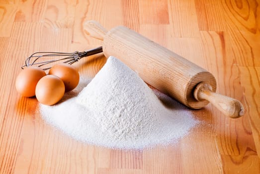Flour with eggs, rolling pin and beater on the wooden table