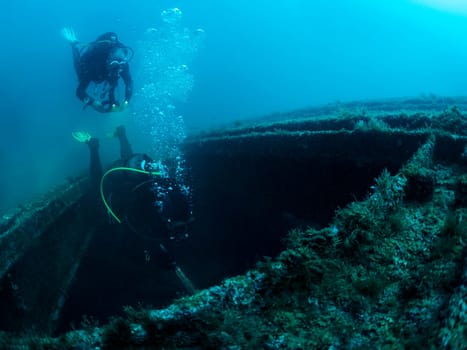 two scuba divers diving into a shipwreck, the water is dark and murky, and the man is surrounded by debris, the scene is eerie and mysterious, with the man exploring the depths of the sunken ship
