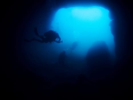 group of scuba divers diving in a dark cave, the cave is filled with water and the people are wearing scuba gear