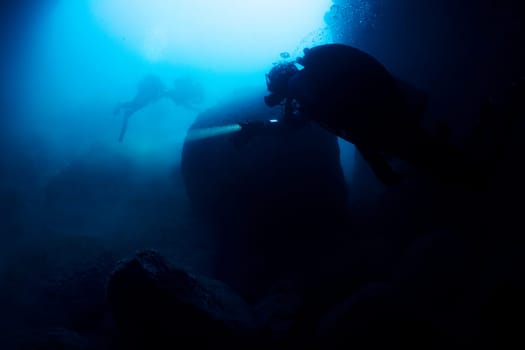 scuba diver diving into the water with a light on, the water is dark blue and the man is wearing a black wetsuit