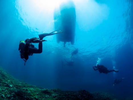 group of people are scuba diving in the ocean, the water is clear and blue, and the sun is shining brightly, the divers are spread out, with some closer to the surface and others deeper in the water