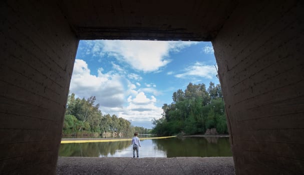 Child boy getting dangerously close to the edge of a river. The boy stands on a concrete edge of the eye of a bridge
