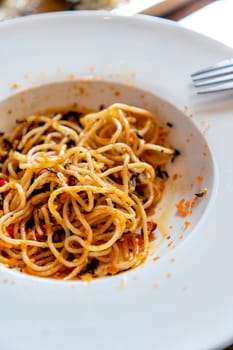 Spaghetti mixed with orange shrimp roe in a white round plate part of it has been eaten There were no vegetables on the plate at all. scattered shrimp roe convey disorder. Selective focus.