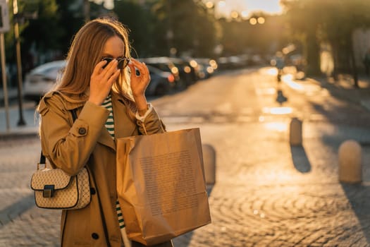 A woman walks around the city after shopping at sunset with a paper bag.