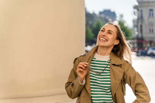 A woman laughs happily and holds glasses in her hand on the street.