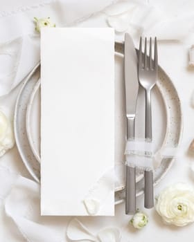 Wedding table setting with card near cream roses and white silk ribbons top view, mockup. Romantic scene with vertical menu card and pastel flowers. Valentines, Spring or Mothers day concept