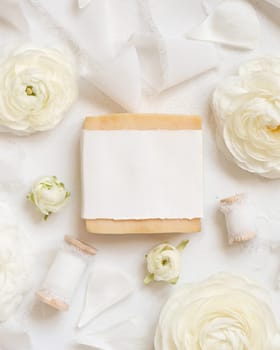 Handmade soap bar with blank label near cream roses and white ribbons top view, soap mockup. Beauty product for face and body care. Natural Spa cosmetic concept