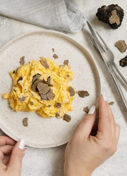 Hands with plate with Scrambled eggs with fresh black truffles top view. Italian cousine, gourmet breakfast