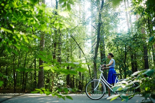 Modern girl with bicycle walking down park