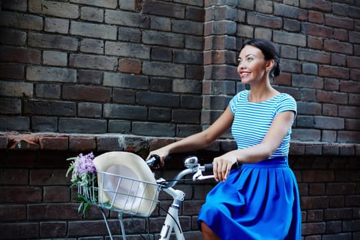 Happy girl dressed in retro style riding bicycle along brick wall