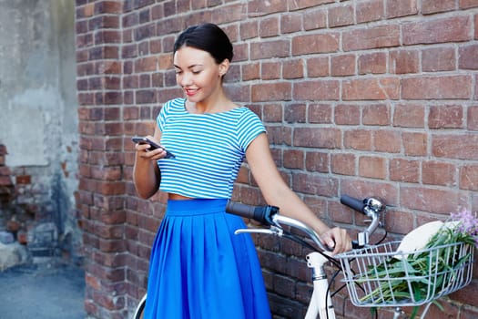 Modern girl dressed in retro style using cellphone against grunge brick wall