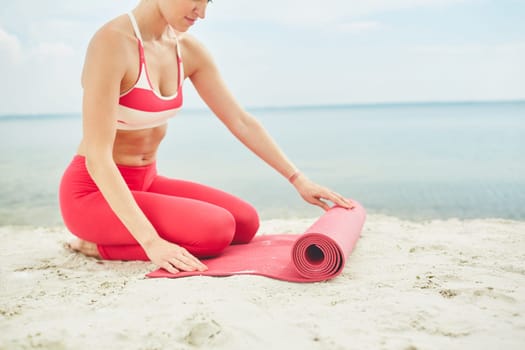 Fit woman unfolding mat before exercising on sandy beach