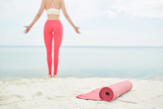 Red rolled mat for yoga on background of young woman standing by water