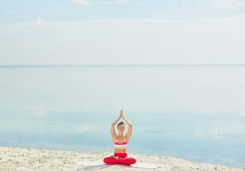 Young woman practicing yoga on sand by water