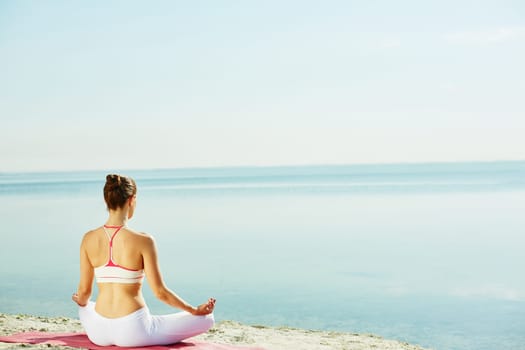 Meditating woman sitting on sandy beach