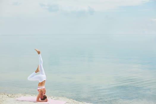 Attractive woman keeping balance while standing on her head on sandy beach