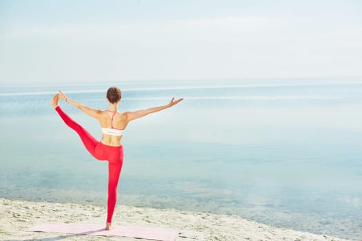 Sporty female in activewear stretching her leg while standing on the beach