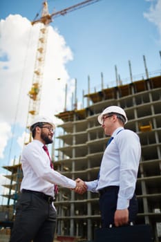 Two confident businessmen handshaking after making agreement on background of building construction