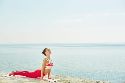 Fit woman doing stretching exercise on mat by water